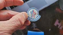Load image into Gallery viewer, Hand holding a Moncler logo close-up with a blurred background