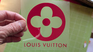 Louis Vuitton logo on a green card held by a hand